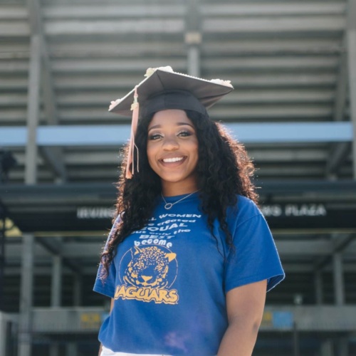 Young woman standing in front of bleachers wearing a graduation cap.